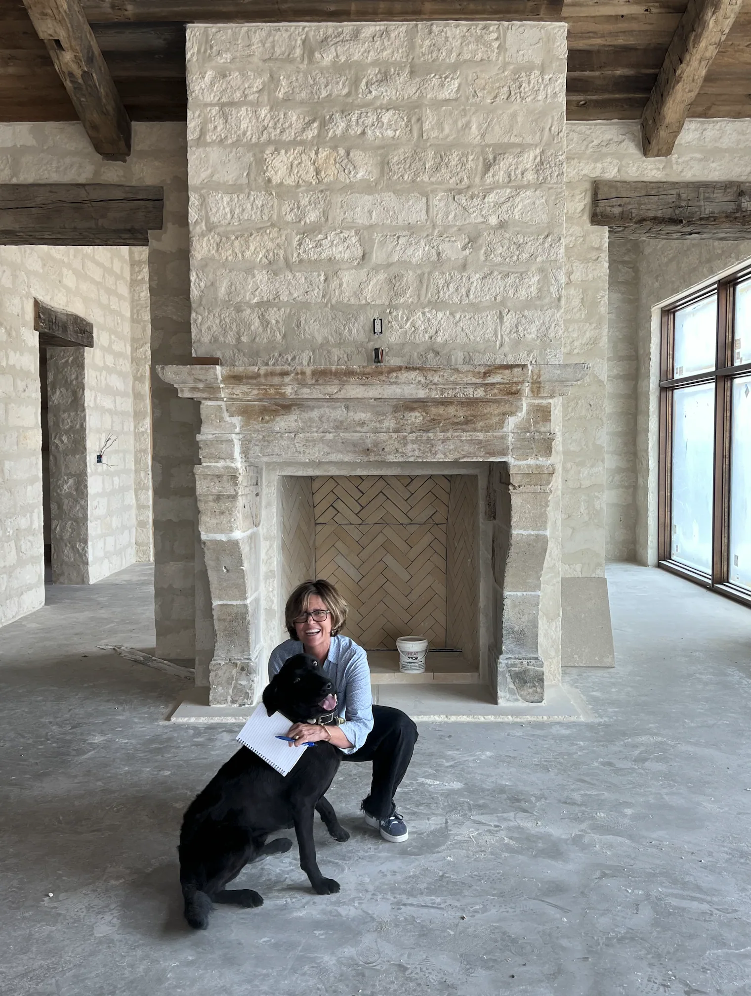 Deborah Kirk on-site at a ranch property, mid-construction, with her dog